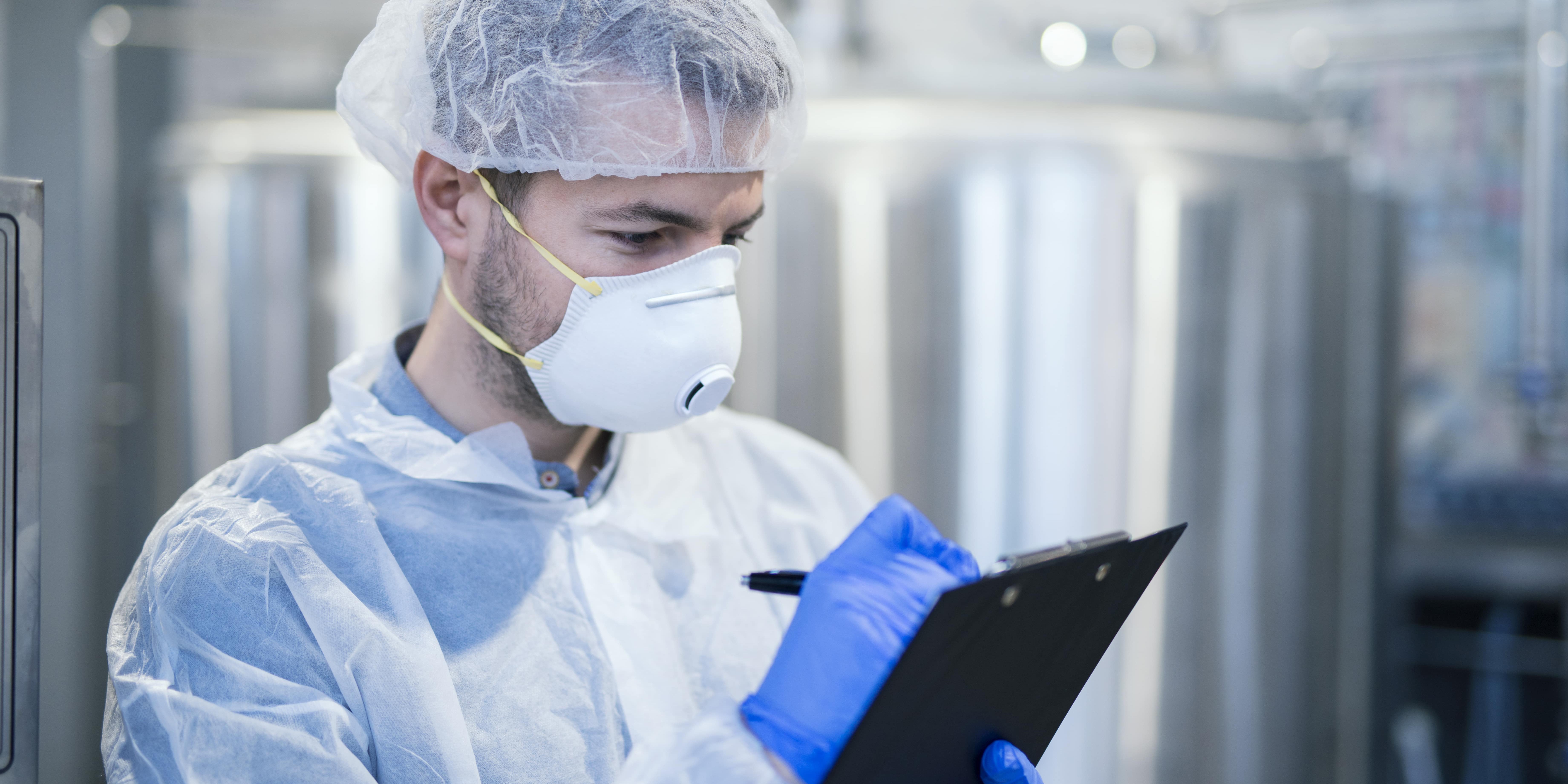 technologist-specialist-with-protective-mask-hairnet-holding-clipboard-checklist-writing-production-results-min-1